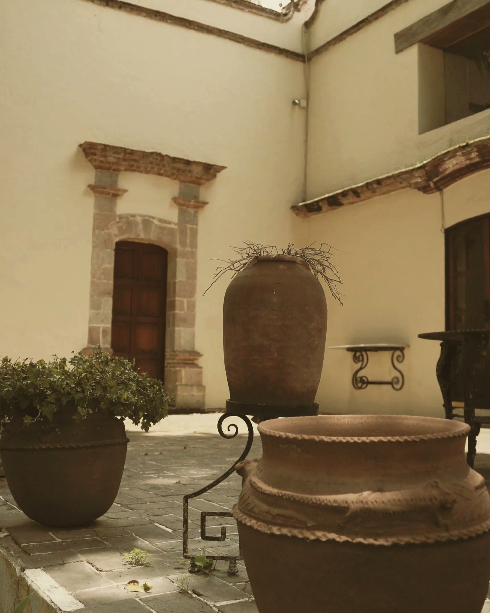 Patio colonial con tinajas de barro y plantas bajo el sol de la tarde